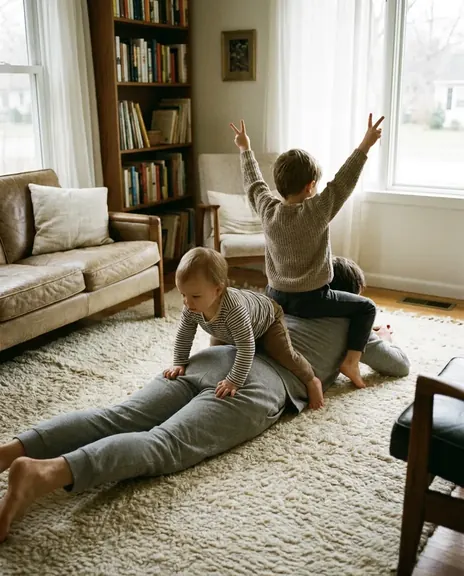 A parent lies face down on a rug; one child climbs on, the other sits on top with arms raised.